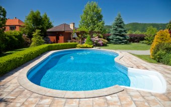 Kidney-shaped swimming pool with sanded brick patio and hedge