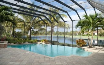 Screen-covered in-ground pool in Florida backyard surrounded by grey brick patio