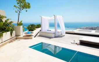 Small lap pool on white patio with a bed pergola overlooking the sea
